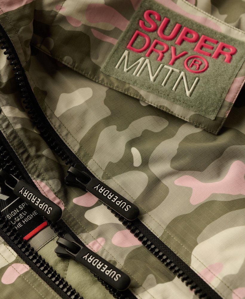 jaqueta corta-vento com capuz para montanha em camuflagem rosa e verde-marinho.