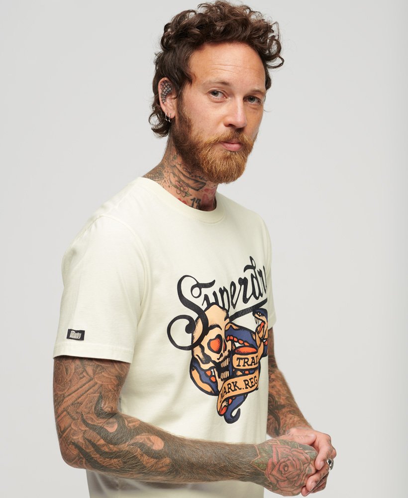 camiseta com estampa frontal de escrita cursiva estilo tatuagem na cor off white.