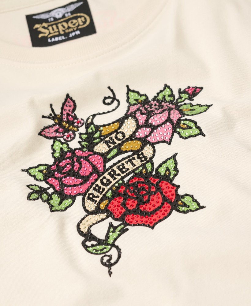 camiseta justa com estampa de tatuagem pequena e strass na cor branca arroz.